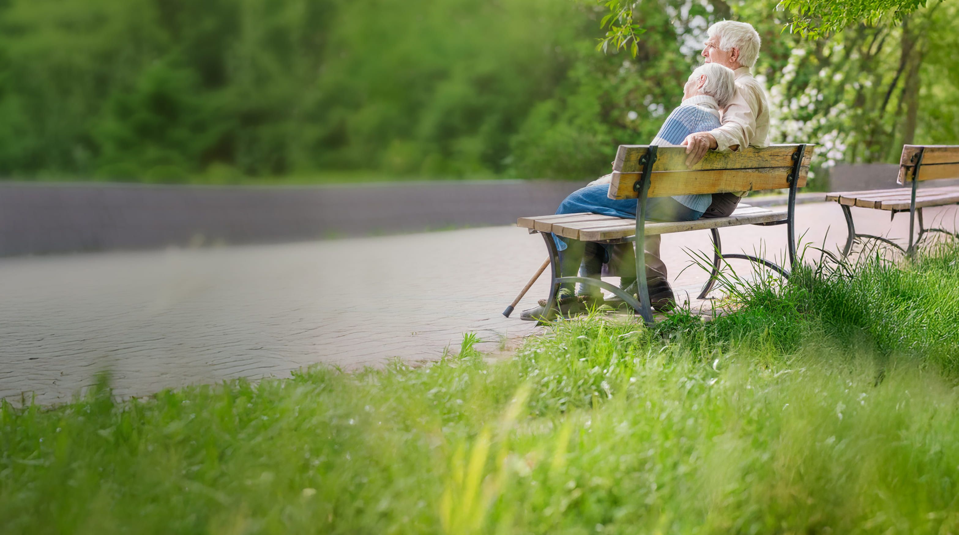 Zwei ältere Menschen sitzen auf einer Bank in einem Park, links ist das Bild verschwommen