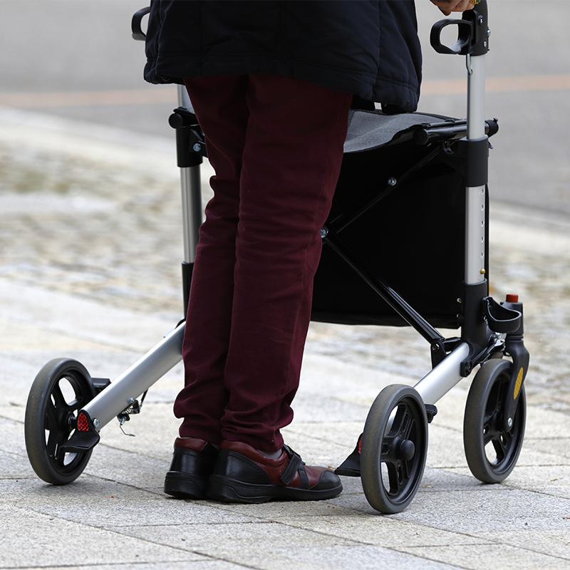 Ältere Frau, die mit ihrer modernen Gehhilfe auf der Straße geht